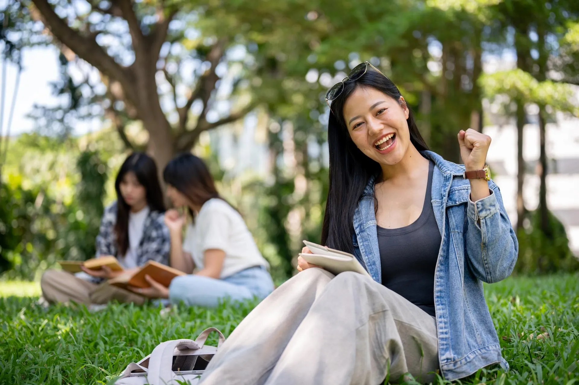 East Asian student smiling on a sunny university campus lawn