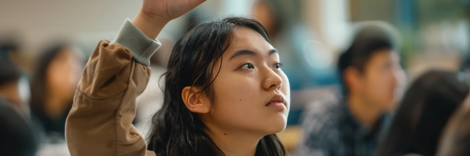 East Asian student raising hand to ask a question in a lecture