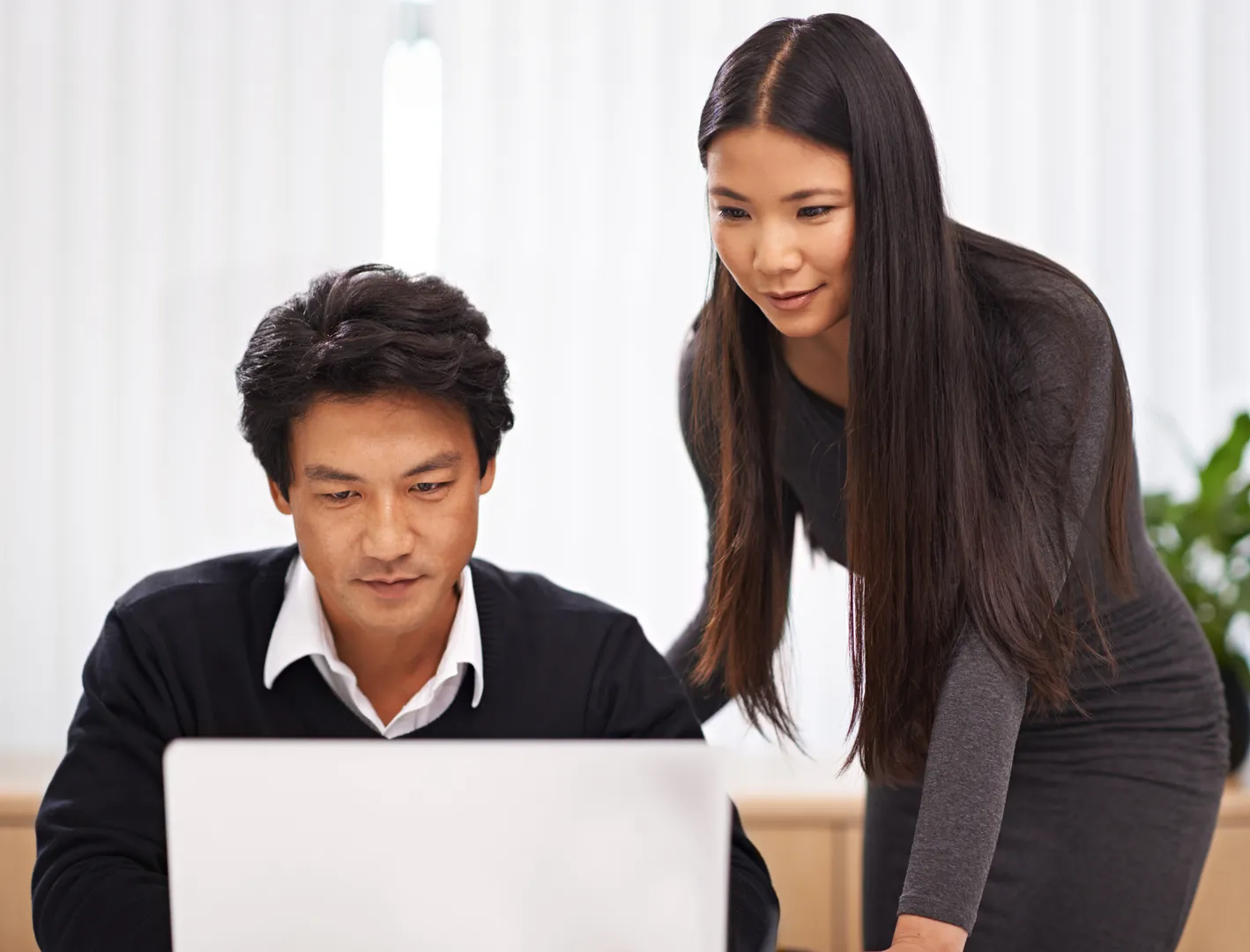 Woman mentoring an East Asian businessman at a laptop in a modern office