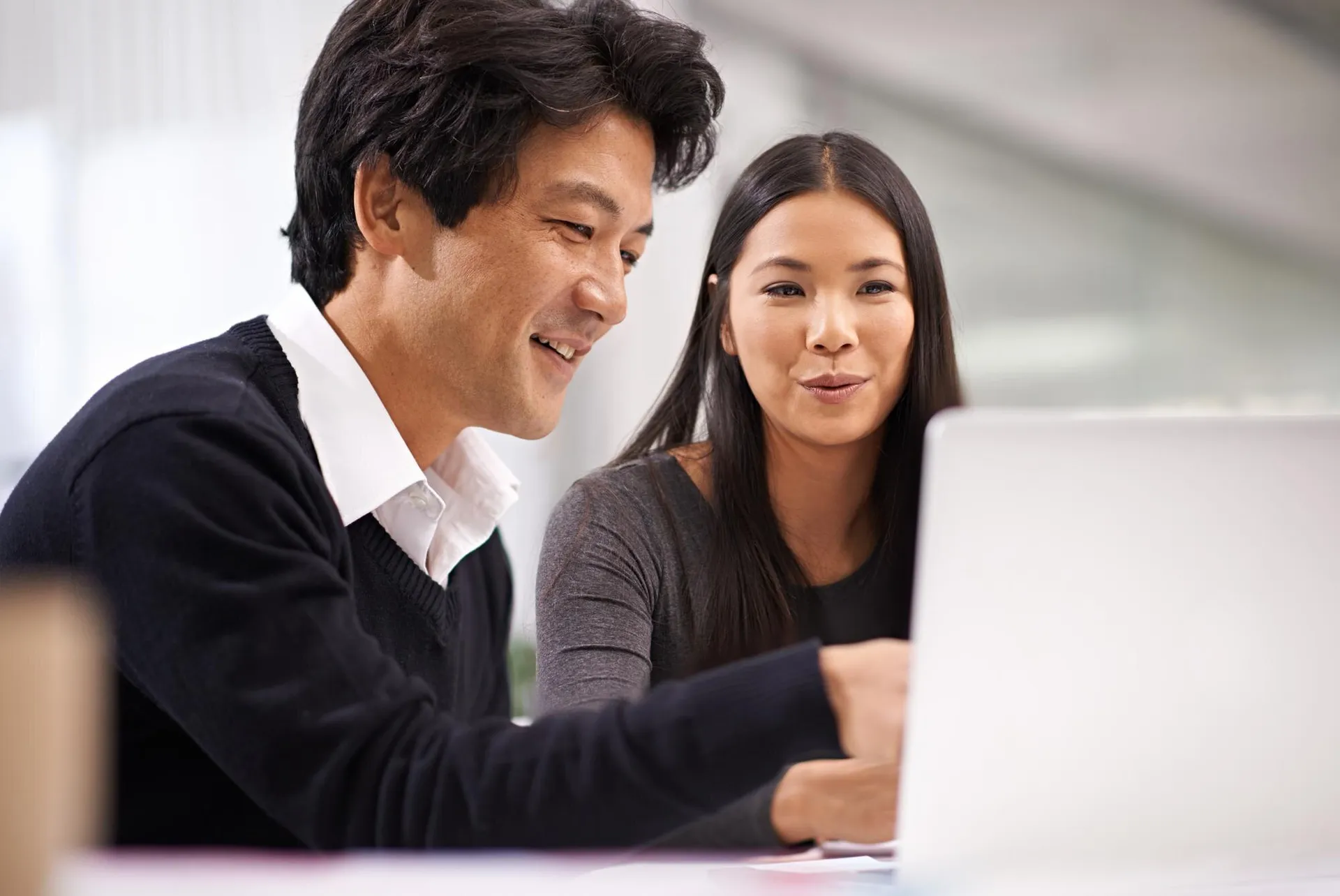 Japanese man and woman collaborating at a laptop in a modern office