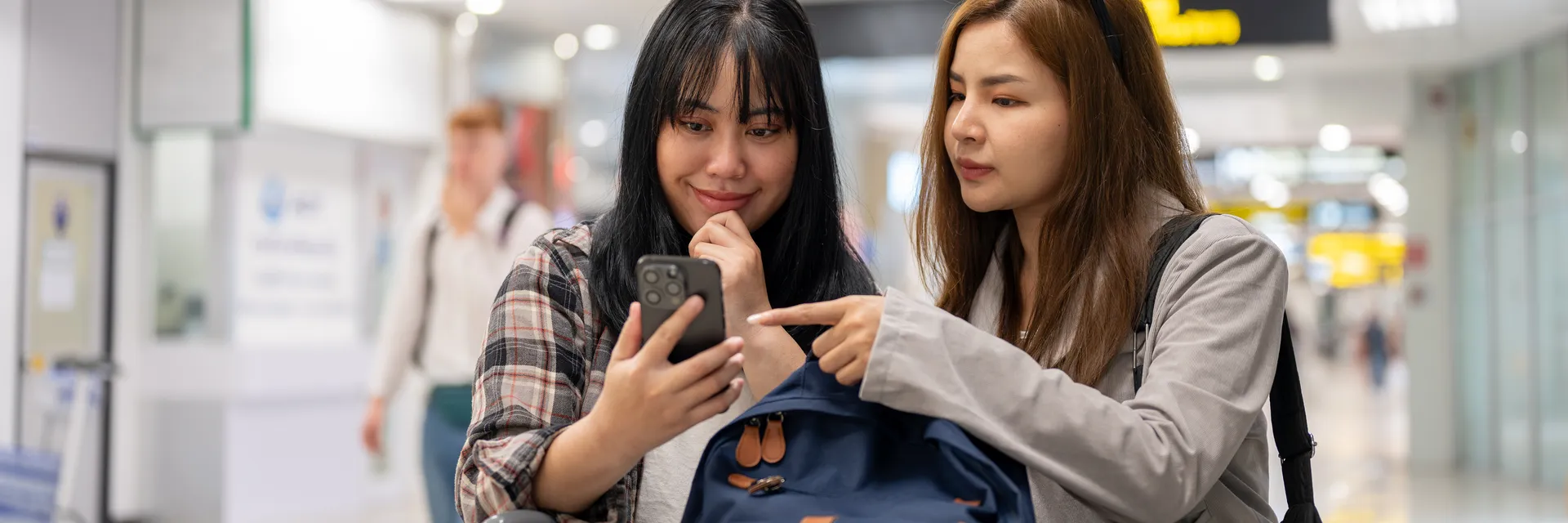 Two East Asian students checking flight information at the airport