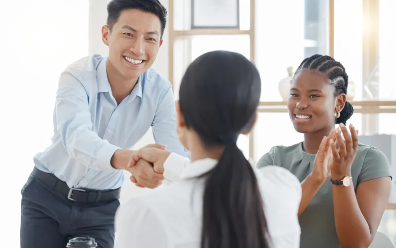 East Asian professional shaking hands with colleagues in an office