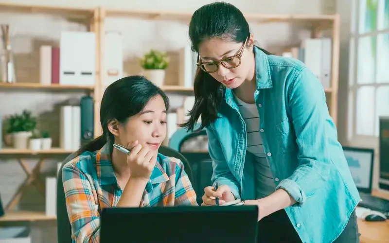 East Asian student adviser guiding a student at a laptop