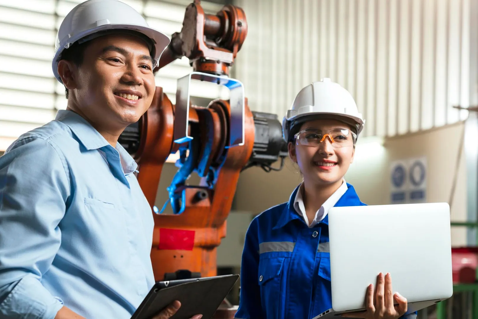 Two Asian engineers inspecting industrial robot systems with a tablet in a manufacturing facility