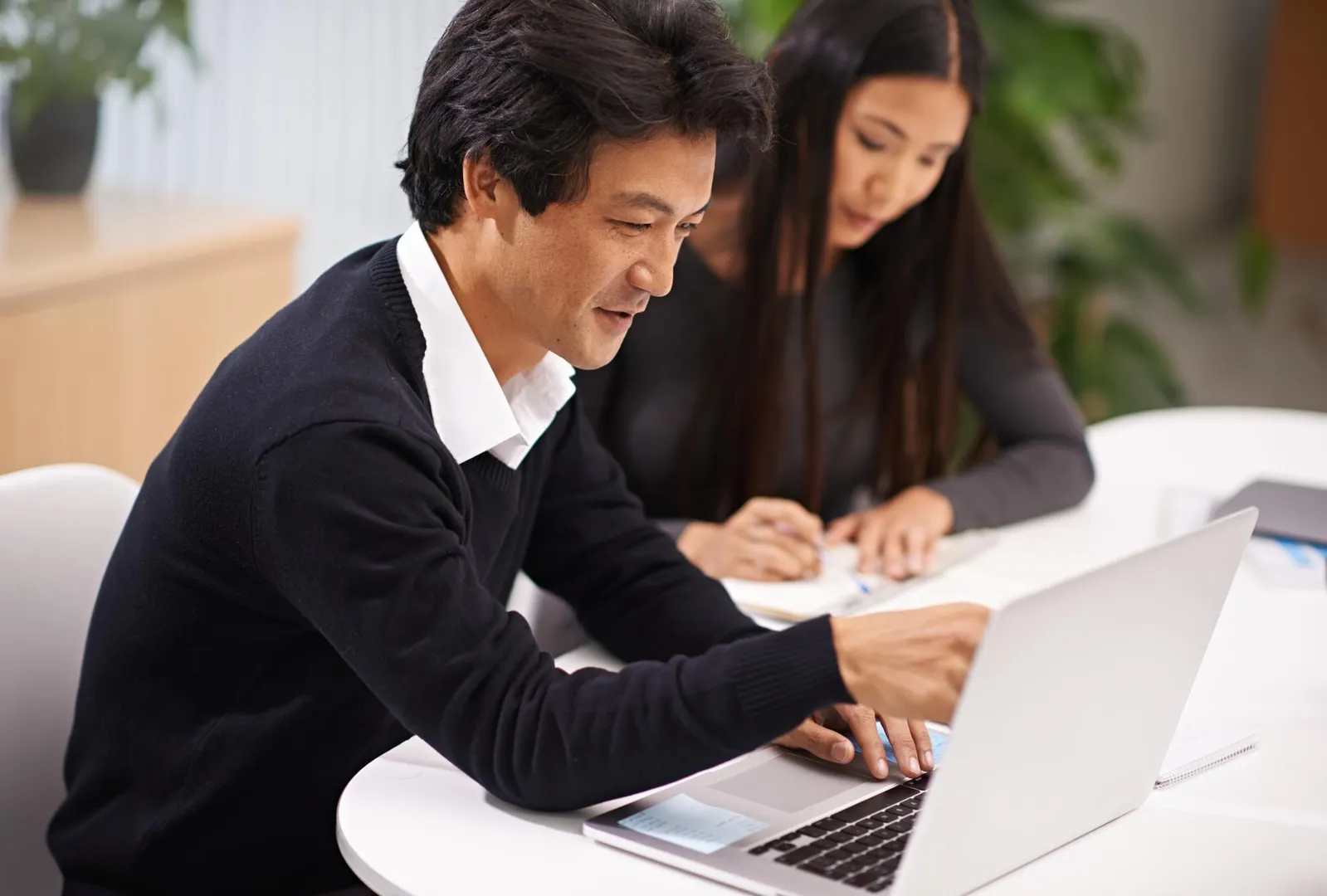 East Asian business professionals collaborating at a laptop in a modern office