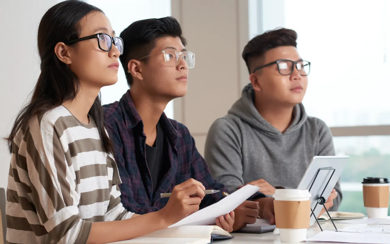 East Asian teenager with laptop in a diverse high school classroom