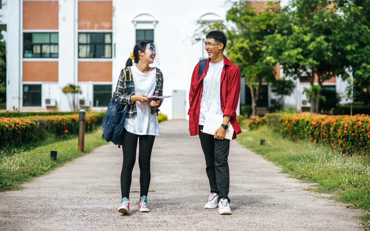 Two Asian students with backpacks walking and laughing on a university campus